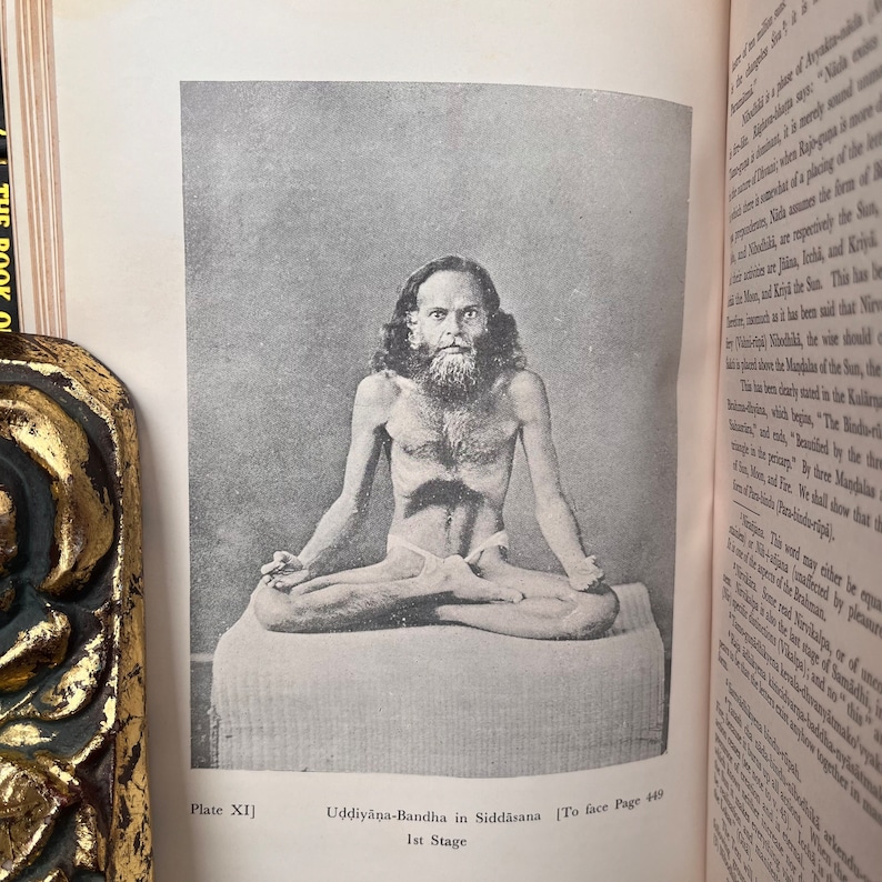 May include: A black and white photograph of a man sitting in a yoga pose. The man is wearing a loincloth and has a long beard. The photo is from a book titled "The Book of Yoga" and the caption reads "Uddiyana-Bandha in Siddhasana 1st Stage".