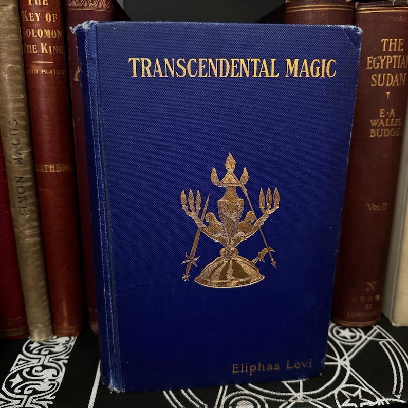May include: A blue hardback book titled "Transcendental Magic" by Eliphas Levi. The book cover features a gold illustration of a candelabra with swords and a helmet.