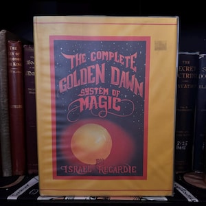 May include: A yellow book with a red and black cover. The title is "The Complete Golden Dawn System of Magic" by Israel Regardie. The cover features a large, orange sun.