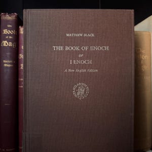May include: A collection of antique books, with the focus on a brown hardcover book titled "THE BOOK OF ENOCH or I ENOCH" by Matthew Black. The book has a New English Edition. Other books are visible in the background.