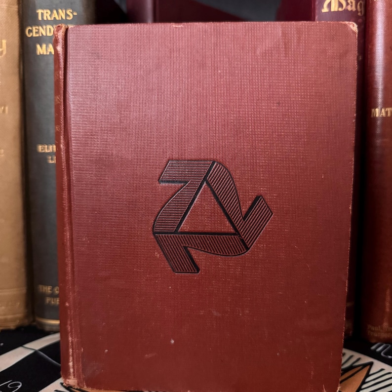 May include: A burgundy hardcover book with a black, three-dimensional, geometric design on the front cover.