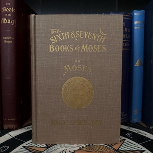 May include: A brown book with gold lettering on the cover. The title is "The Sixth & Seventh Books of Moses or Moses Magic, Spirits and Art".