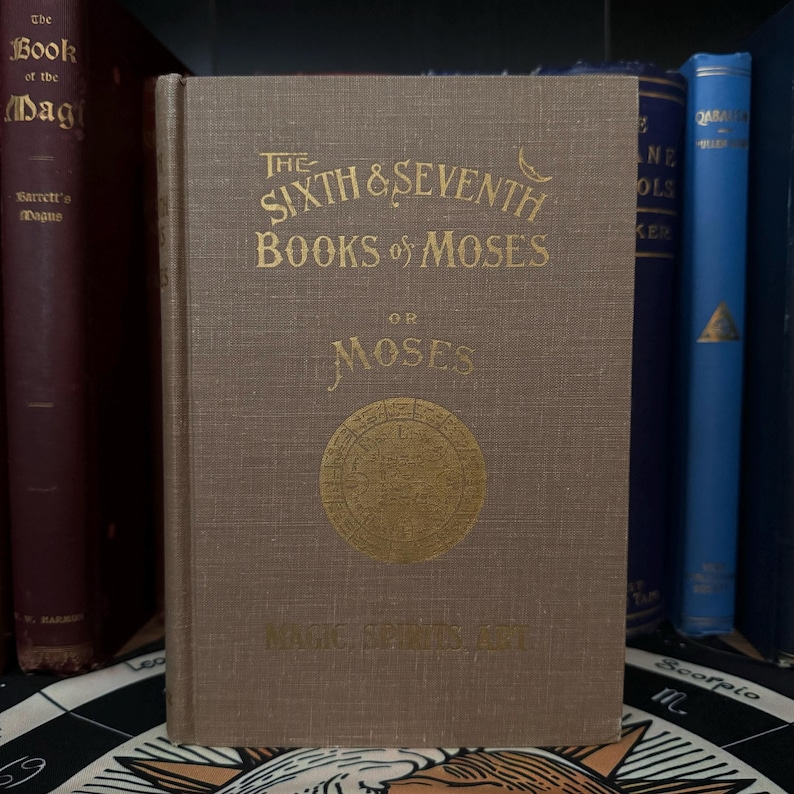 May include: A brown book with gold lettering on the cover. The title is "The Sixth & Seventh Books of Moses or Moses Magic, Spirits and Art".