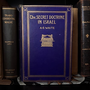 Puede incluir: Un libro de tapa dura titulado The Secret Doctrine in Israel de A.E. Waite con una cubierta azul oscuro, letras doradas y una ilustración central dorada de dos figuras aladas a ambos lados de un altar, enmarcado por líneas doradas.
