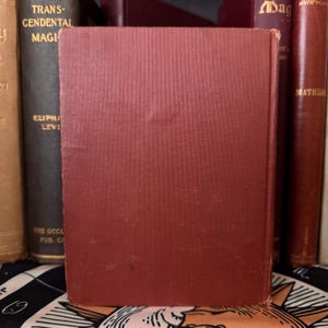 May include: A red hardcover book with the title "Transcendental Magic" by Eliphas Levi. The book is on a shelf with other books.