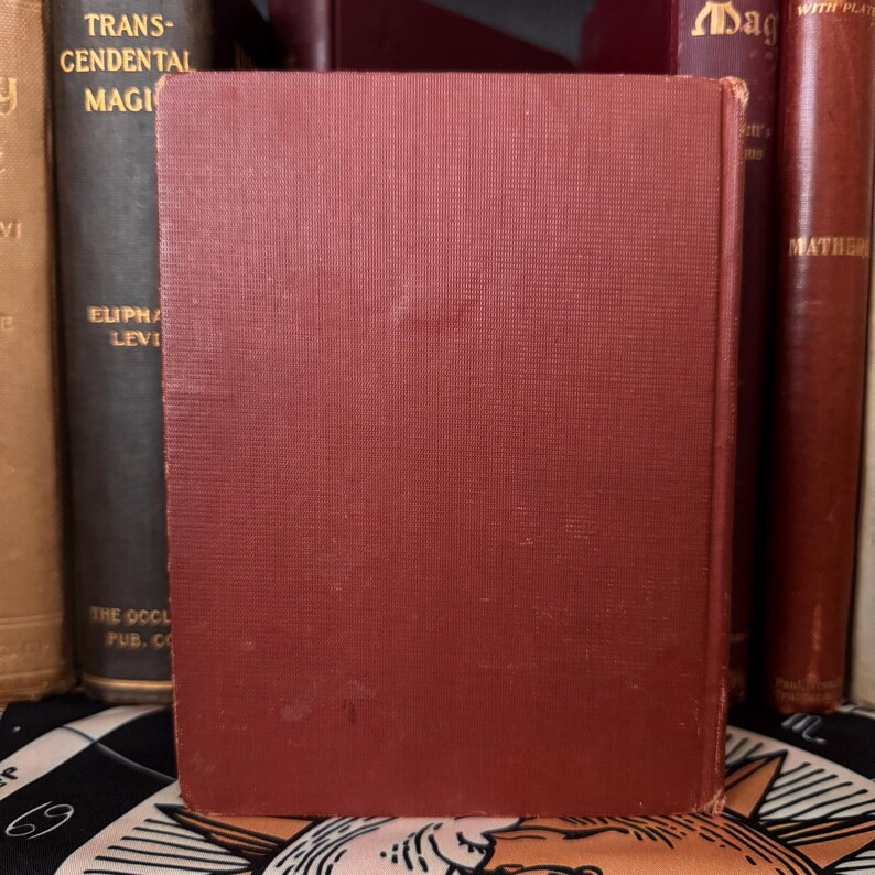 May include: A red hardcover book with the title "Transcendental Magic" by Eliphas Levi. The book is on a shelf with other books.