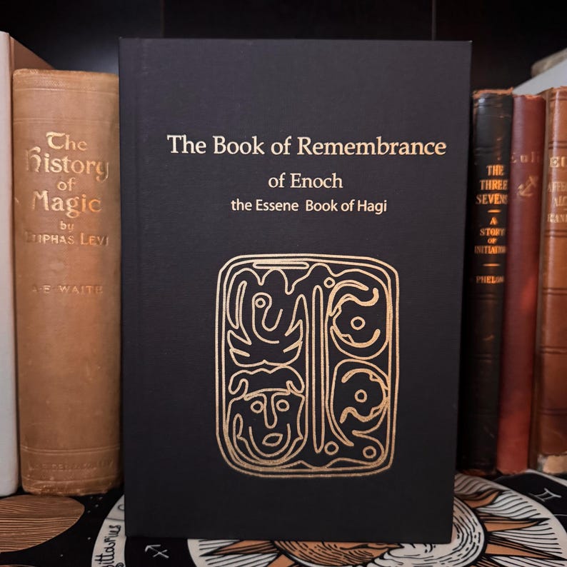 May include: A black book titled "The Book of Remembrance of Enoch" with gold lettering and an ornate gold design. The book is standing upright on a shelf with other antique books. The book's cover features the text "the Essene Book of Hagi".