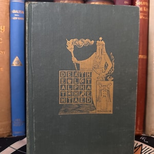 May include: A vintage, dark green book with gold lettering and illustrations. The cover features a figure holding a torch and the words "DEATH, ELT, ALPHA, THRE, HTAED." Other books are visible in the background.