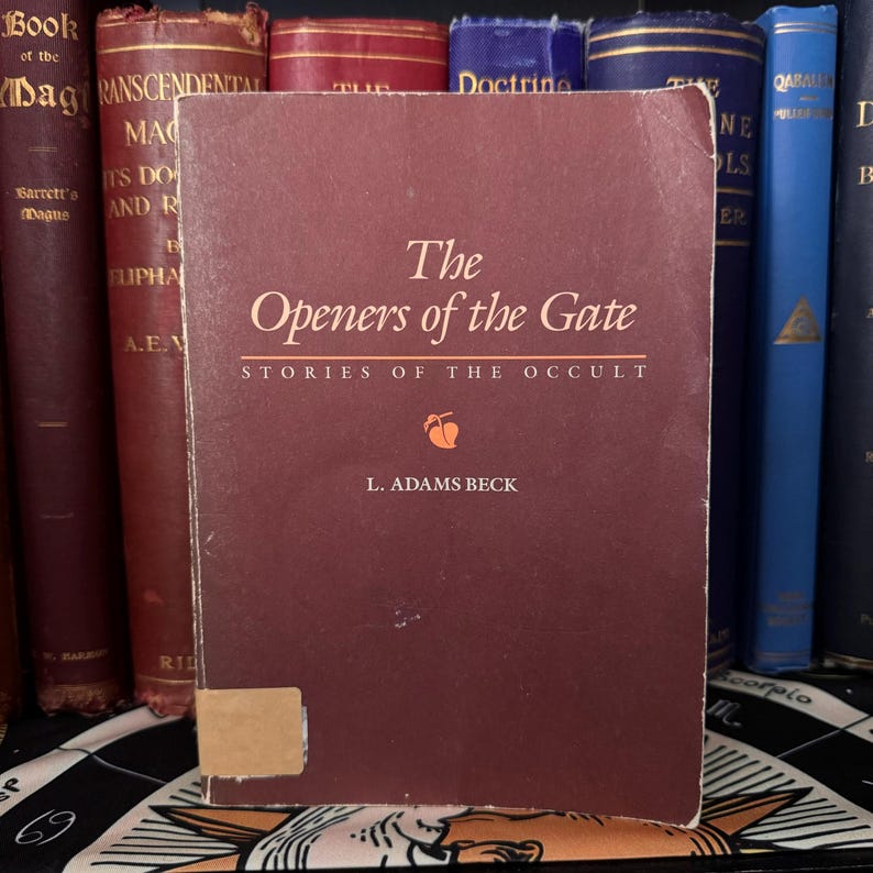 以下が含まれることがあります： L. アダムズ・ベック著「The Openers of the Gate」というタイトルのワインレッドのハードカバーの本。副題は「Stories of the Occult」。本は他の本と一緒に棚に置かれている。