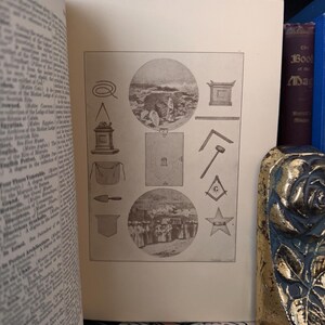 Puede incluir: Un libro abierto muestra una ilustraci&oacute;n detallada con varios s&iacute;mbolos e im&aacute;genes circulares. La p&aacute;gina presenta dibujos de herramientas, formas geom&eacute;tricas y elementos arquitect&oacute;nicos, todos en blanco y negro. Las p&aacute;ginas del libro est&aacute;n envejecidas, lo que sugiere un art&iacute;culo vintage o antiguo.