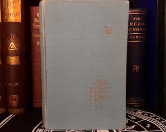 May include: A light blue hardback book with a silver design on the front cover. The book is on a shelf with other books.