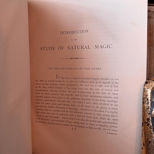 Puede incluir: P&aacute;ginas de un libro abierto con texto de "Study of Natural Magic". El texto incluye los t&iacute;tulos "Introduction" y "Of the Influences of the Stars". Las p&aacute;ginas est&aacute;n envejecidas con un tono c&aacute;lido y amarillento, lo que sugiere un libro antiguo.