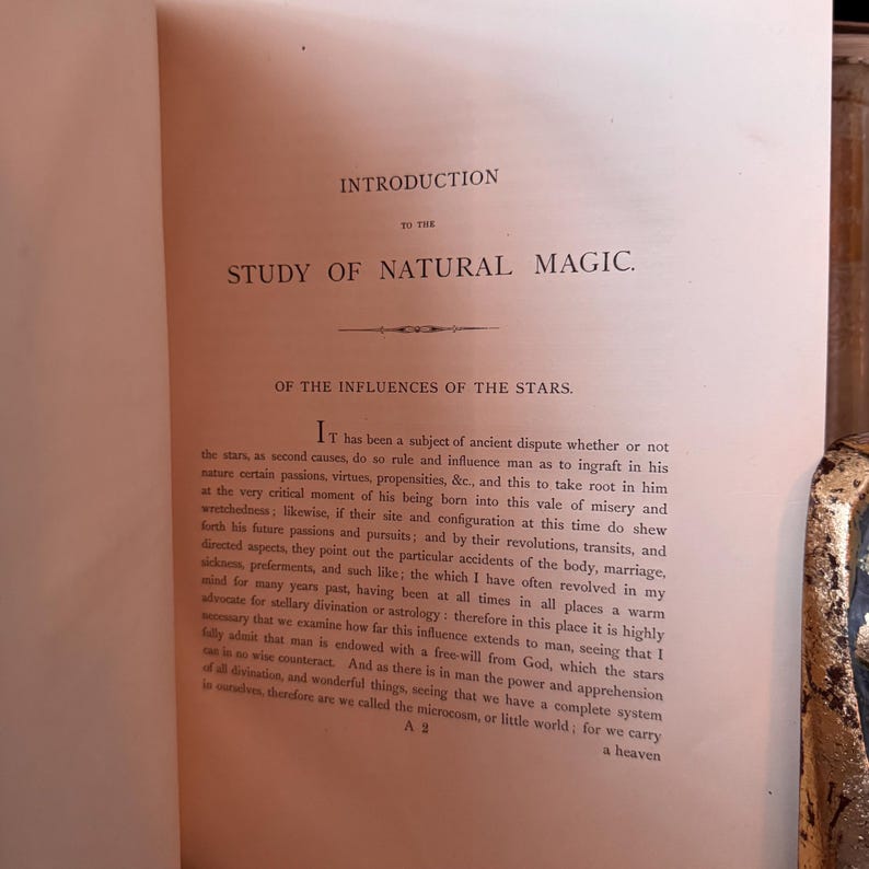 Puede incluir: P&aacute;ginas de un libro abierto con texto de "Study of Natural Magic". El texto incluye los t&iacute;tulos "Introduction" y "Of the Influences of the Stars". Las p&aacute;ginas est&aacute;n envejecidas con un tono c&aacute;lido y amarillento, lo que sugiere un libro antiguo.