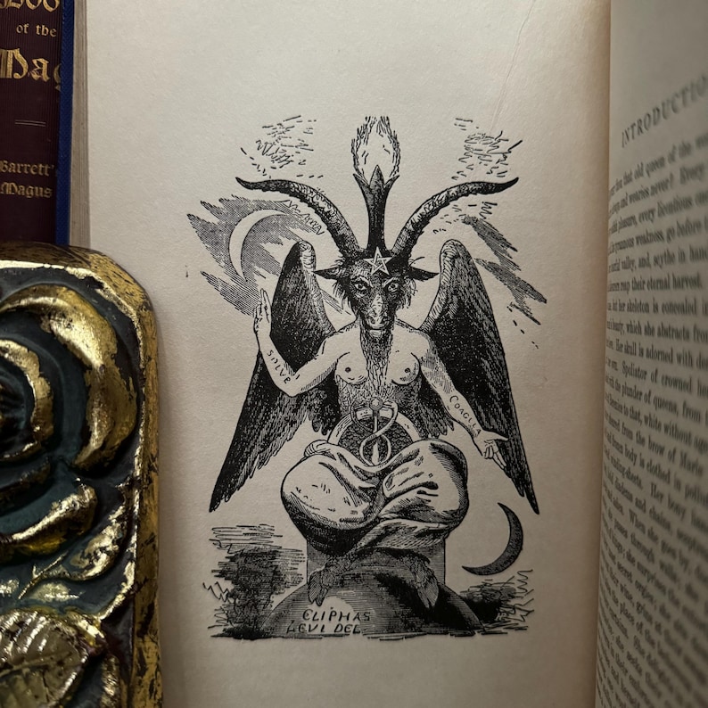 May include: A black and white illustration of a goat-like figure with horns and wings. The figure is sitting on a throne with a pentagram on its head. The text "CLIPPAS LEVI DEL" is written below the figure.