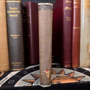 Pu&ograve; includere: Un libro vintage intitolato "The Occult World" di A.P. Sinnett. Il libro &egrave; rilegato in carta marrone con lettere dorate e un design decorativo sul dorso.