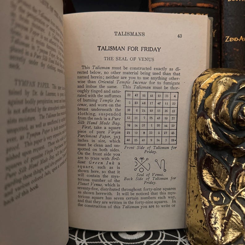 May include: A page from a book about talismans, showing a talisman for Friday, the Seal of Venus. The talisman is a square with a symbol inside, and the page includes instructions for creating the talisman, including the use of parchment paper, green ink, and a specific size. The page also includes a table of numbers.