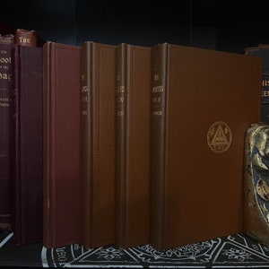 Könnte beinhalten: Vier braune, ledergebundene Bücher mit goldenen Beschriftungen auf den Rückseiten. Die Bücher sind betitelt mit "The States Vol. I", "The States Vol. II", "The States Vol. III" und "The States Vol. IV". Die Bücher sind in einer Reihe auf einem Regal angeordnet. Das Buch ganz rechts hat ein goldenes Emblem auf dem Einband.