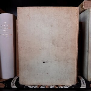 May include: A stack of antique books with aged, off-white covers. The spine of one book displays the title "THE BOOK OF CEREMONIAL MAGIC" in gold lettering. The books are arranged on a shelf, suggesting a collection of vintage literature.