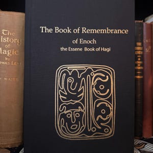 May include: A black book titled "The Book of Remembrance of Enoch" with gold lettering and an intricate gold design. The book is part of a collection of antique books, with a tan book on the left and other books on the right.