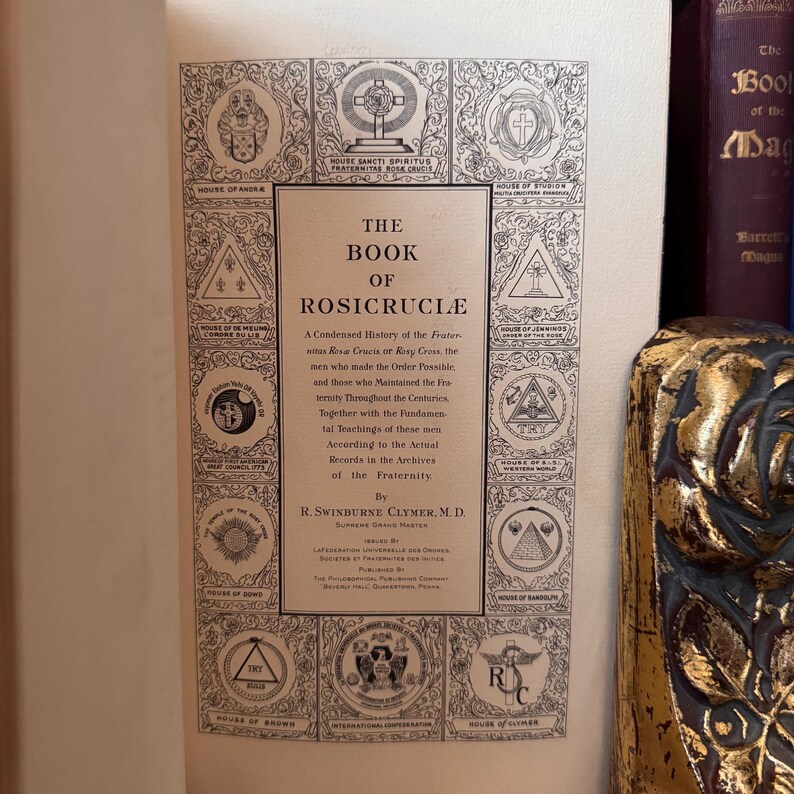Może przedstawiać: Antyczna książka zatytułowana "The Book of Rosicrucia" z kr&oacute;tką historią Zakonu R&oacute;żokrzyżowc&oacute;w. Okładka zawiera ozdobny wz&oacute;r z symbolami i tekstem.