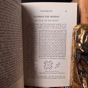 May include: Open book page featuring a detailed illustration of a talisman for Monday, with text and a numerical grid. The page is from an antique book, with a gold-colored decorative element visible on the right side.