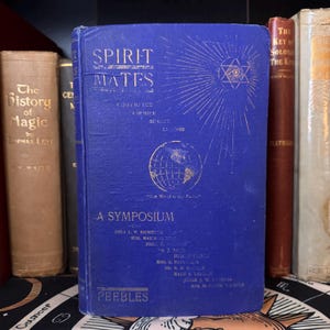 May include: A blue hardback book titled "Spirit Mates: A Symposium" with gold lettering and illustrations. The book cover features a globe, a star with an eye in the centre, and the text "The World is to My Father."