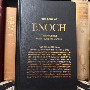 May include: A hardcover book titled "THE BOOK OF ENOCH THE PROPHET" with gold lettering on a black cover. The book is translated by Richard Laurence. Other books are visible in the background.