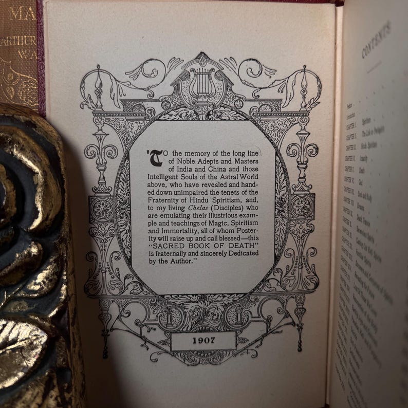 May include: An open book page with ornate black and white illustrations and text. The text includes the title "SACRED BOOK OF DEATH" and the year 1907. The page is from a vintage book with a gold-colored decorative edge.