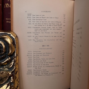 May include: A page from a vintage book titled "Palmistry" with a table of contents listing chapters on the lines of the hand, physiognomy, and the wheel of Pythagoras. The book is printed on cream-colored paper with black ink.