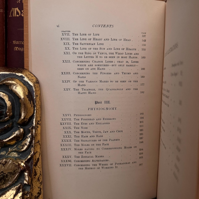 May include: A page from a vintage book titled "Palmistry" with a table of contents listing chapters on the lines of the hand, physiognomy, and the wheel of Pythagoras. The book is printed on cream-colored paper with black ink.