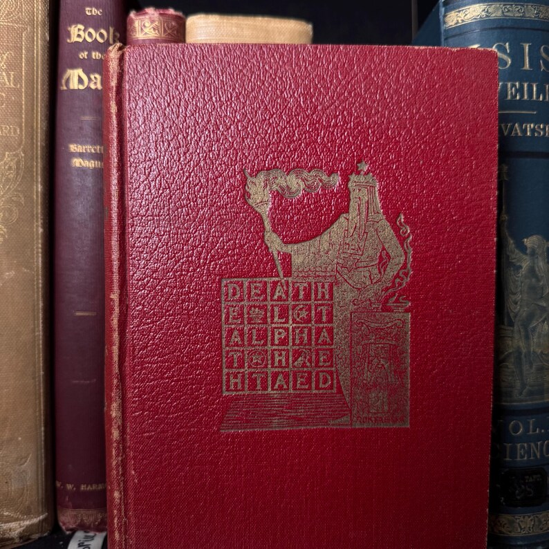 May include: A red book with gold lettering and a detailed illustration on the cover. The cover text includes the words "DEATH," "ALPHA," and "HTAED." The book is part of a collection of antique books.