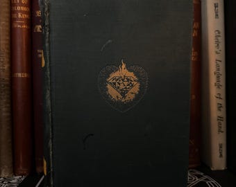 May include: A dark green hardcover book with a gold-colored diamond design on the front cover. The diamond is surrounded by a heart shape and has a flame above it. The book title is "Cheiro's Language of the Hand."
