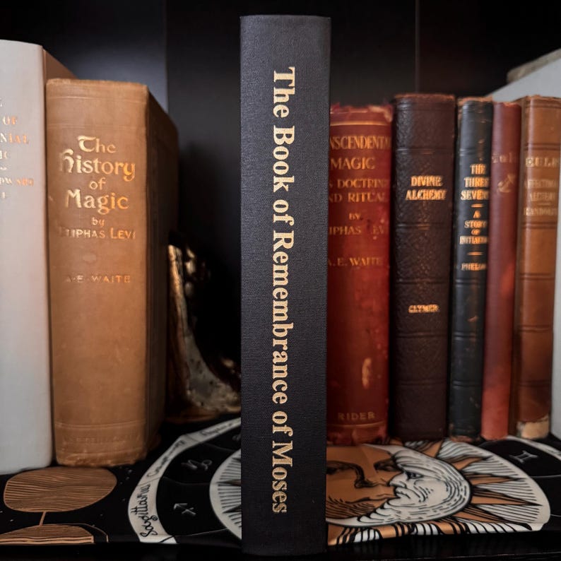 Peut inclure: Un livre noir intitul&eacute; "The Book of Remembrance of Moses" avec des lettres dor&eacute;es est pr&eacute;sent&eacute; parmi d'autres livres anciens. La tranche est visible, affichant le titre. Les livres sont sur une &eacute;tag&egrave;re, sugg&eacute;rant une collection de litt&eacute;rature historique ou occulte.