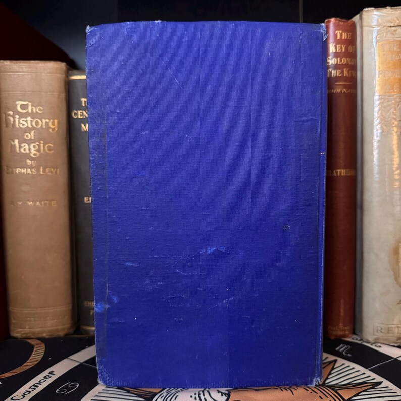 May include: A blue hardcover book with the title "The Key of Solomon the King" printed in gold lettering on the spine. The book is on a shelf with other books.