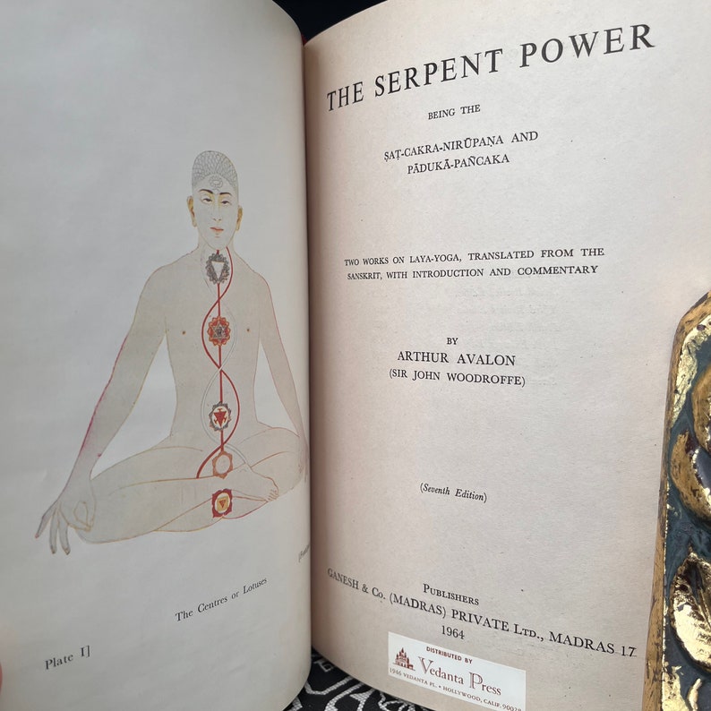 May include: A vintage book cover featuring a red and white illustration of a person sitting in a yoga pose. The book title is "The Serpent Power" and the author is "Arthur Avalon (Sir John Woodroffe)".