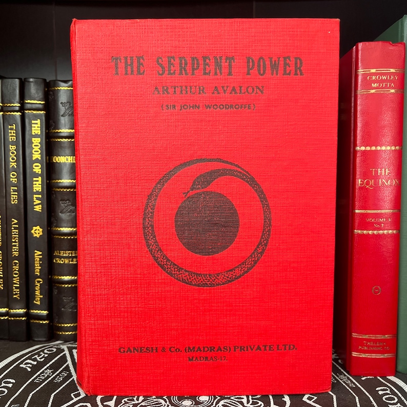 May include: A red hardback book titled "The Serpent Power" by Arthur Avalon (Sir John Woodroffe). The book cover features a black and white illustration of a snake coiled around a circle. The book is published by Ganesh & Co. (Madras) Private Ltd. Madras-17.
