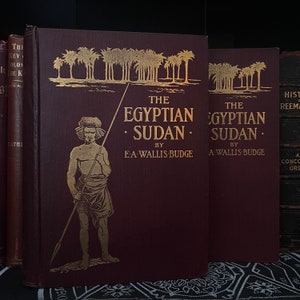 Könnte beinhalten: Zwei antike gebundene Bücher mit goldenen Lettern auf einem dunkelburgunderfarbenen Einband. Die Bücher tragen den Titel "The Egyptian Sudan" von E.A. Wallis Budge und "The Egyptian Sudan" von A. Wallis Budge. Der Einband des Buches links zeigt eine Schwarzweißillustration eines Mannes mit einer Lanze.