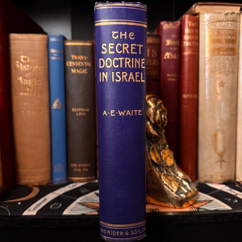May include: A shelf of old books, with a prominent dark blue volume titled "The Secret Doctrine in Israel" by A.E. Waite. The gold lettering contrasts with the blue cover. Other books in the background have different colors and titles, creating a vintage look.