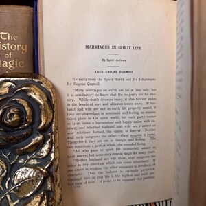 May include: A vintage book with a gold-leaf embossed rose design on the cover. The book is open to a page titled "Marriages in Spirit Life" and includes text about true unions formed in the spirit world. The text discusses the nature of marriage in the afterlife and how it differs from earthly unions.