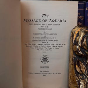 May include: A vintage book titled "The Message of Aquaria: The Significance and Mission of the Aquarian Age" by Harriette Augusta Curtiss and F. Homer Curtiss. The book is a second edition published in 1923 by The Curtiss Philosophic Book Co. in San Francisco.