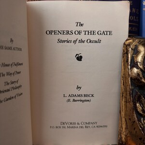 以下が含まれることがあります： 「The Openers of the Gate: Stories of the Occult」というタイトルの書籍の表紙。L. アダムズ・ベック（E. バリントン）著。表紙は白で、黒い文字と、葉のついた果物の小さな黒いイラストが描かれている。