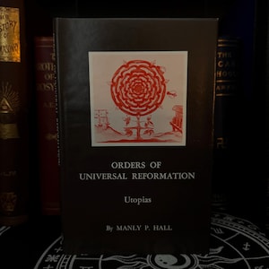 Op de afbeelding: Een zwart boek met een rode roos illustratie op de omslag. De titel is "Orders of Universal Reformation: Utopias" door Manly P. Hall.