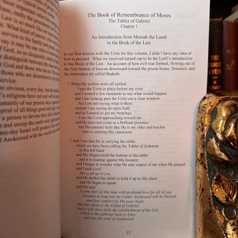 Peut inclure: Livre ouvert avec le texte &laquo; Le Livre du Souvenir de Mo&iuml;se &raquo; et &laquo; La Tablette de Gabriel &raquo;. Le texte est en anglais. Un objet d&eacute;coratif dor&eacute; et noir est au premier plan.