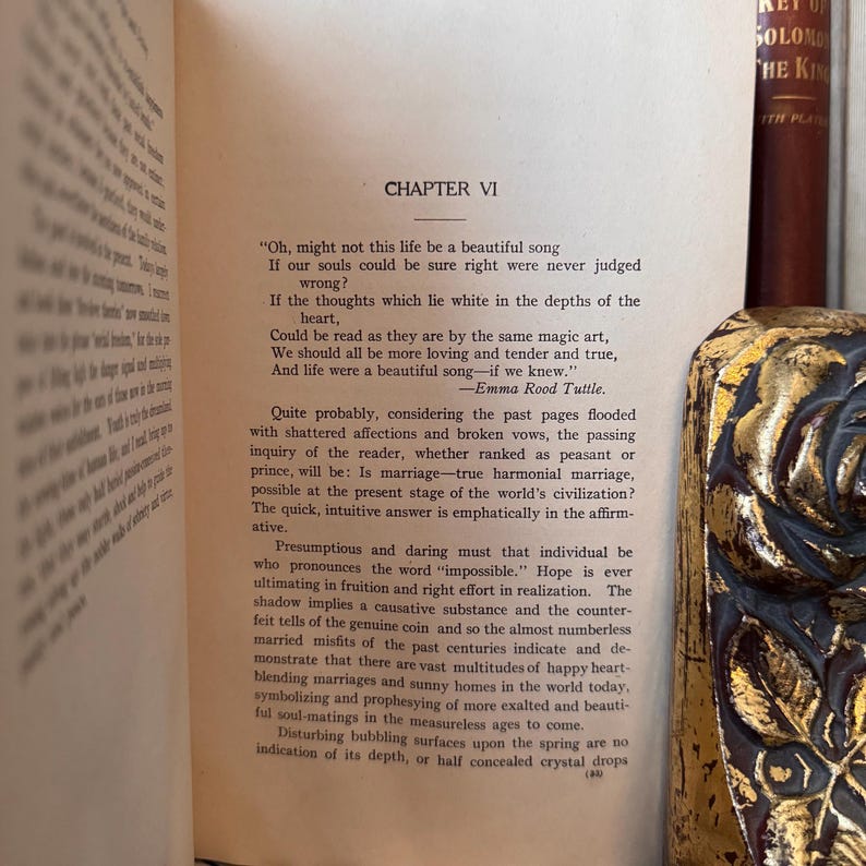 May include: A page from a vintage book with a chapter titled "Chapter VI" and a quote about life being a beautiful song. The text is printed in black ink on white paper. The book is open to a page with a brown leather cover.