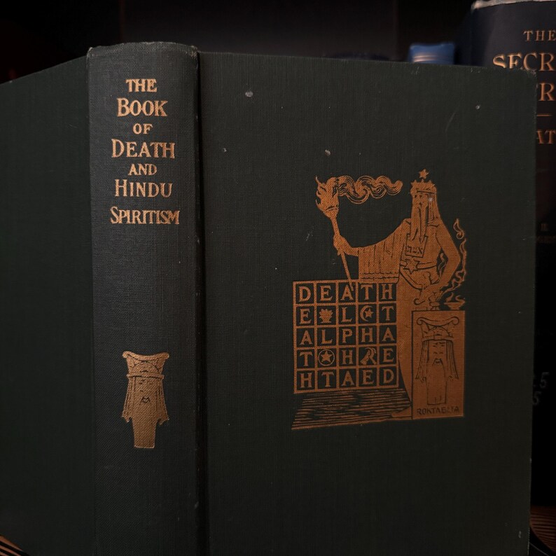 May include: The Book of Death and Hindu Spiritism, a dark green hardcover book with gold lettering and an illustration of a figure holding a torch and a grid with the word "DEATH" in it.