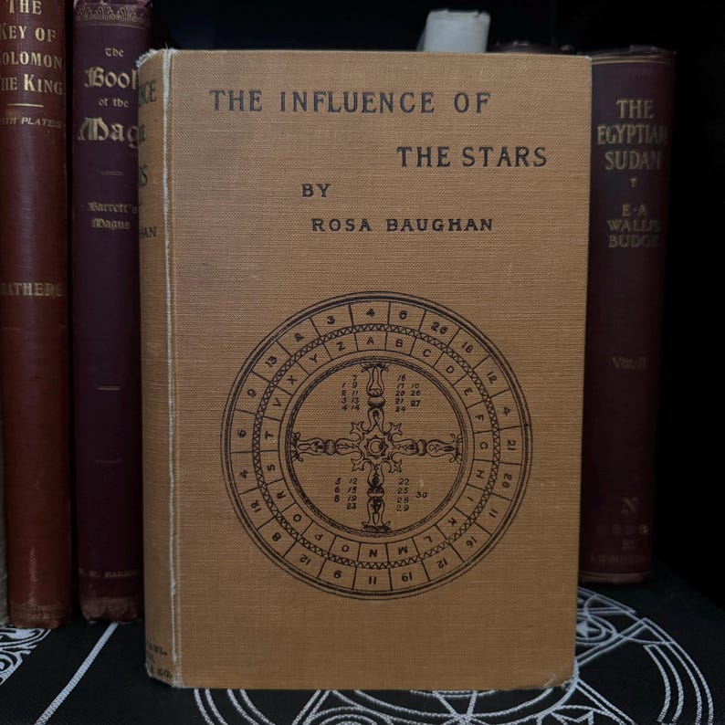 May include: A vintage book titled "The Influence of the Stars" by Rosa Baughan. The cover features a brown background with a black circular design containing letters and numbers.