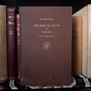 May include: A brown hardcover book titled "THE BOOK OF ENOCH or I ENOCH" by Matthew Black. The book has a textured cover and is part of a collection of antique books. The title and author are in a serif font.