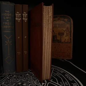 May include: A collection of vintage books with brown and blue covers. The books are titled "The Hidden Life in Free-Masonry" by Leadbeater, "The Light of Egypt" Vol. I, and "The Light of Egypt" Vol. II. The books are sitting on a black surface with a white design.