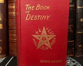 May include: A red hardback book titled "The Book of Destiny" with a gold five-pointed star and the words "Grand Orient" on the front cover.