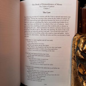 Peut inclure: Livre ouvert avec le titre "Le Livre du Souvenir de Mo&iuml;se" et "La Tablette de Gabriel". Le texte d&eacute;crit une session avec l'Urim et la Loi de Jeshurun. Le num&eacute;ro de page 179 est visible.